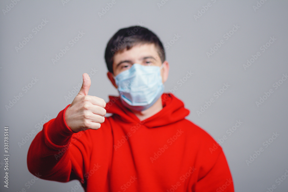 young man in red sweatshirt wearing a protective mask on his face and showing a finger up, concept health, gesture optimistic outlook in future, survivor behavior young man in red sweatshirt wearing a protective mask on his face and showing a finger up, concept health, gesture optimistic outlook in future, survivor behavior