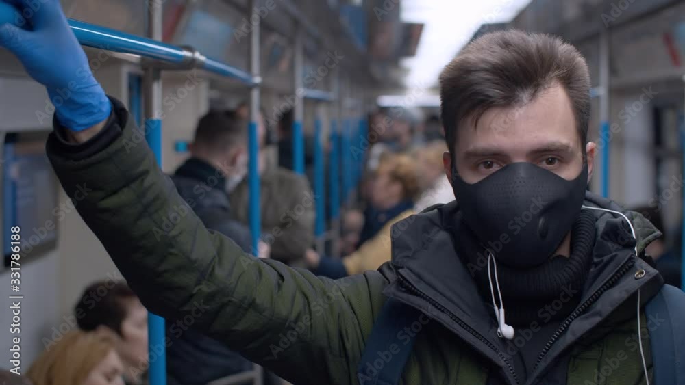 Close up portrait of a young man in reusable protective mask inside subway car. Blurry passengers. Coronavirus epidemic Precautions. Healthy lifestyle concept. COVID-19 pandemic Close up portrait of a young man in reusable protective mask inside subway car. Blurry passengers. Coronavirus epidemic Precautions. Healthy lifestyle concept. COVID-19 pandemic