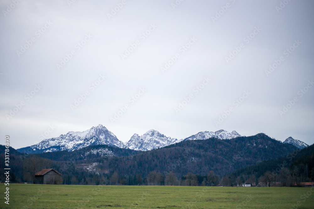 Alpine mountains with snowy peaks. Old european houses. Blue sky with clouds.