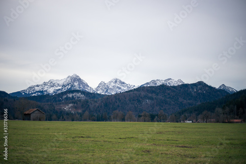 Alpine mountains with snowy peaks. Old european houses. Blue sky with clouds.