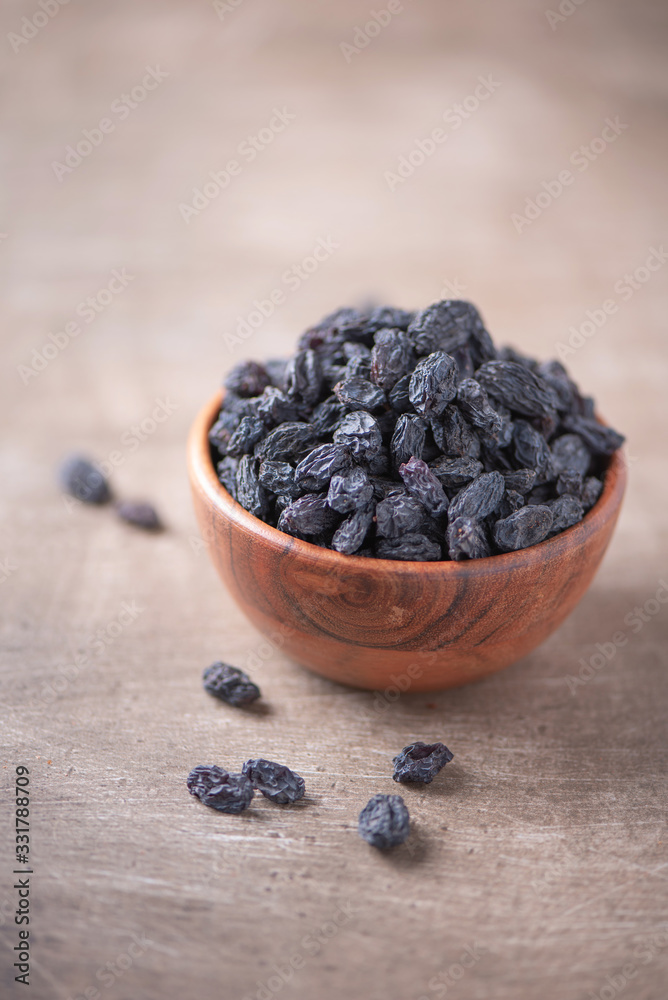 Black raisins in wooden bowl on wood textured background. Copy space. Superfood, vegan, vegetarian food concept. Macro of fresh sweet raisin, selective focus. Healthy snack Black raisins in wooden bowl on wood textured background. Copy space. Superfood, vegan, vegetarian food concept. Macro of fresh sweet raisin, selective focus. Healthy snack