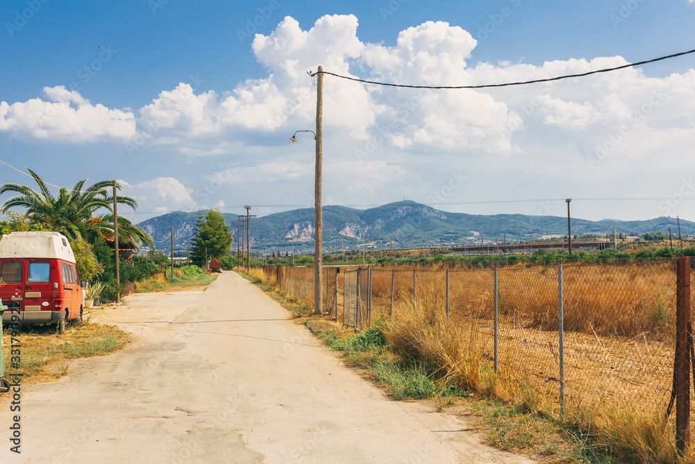 Empty rural road going through prairie under cloudy sky in Greece, Corinth. Vintage style processing image.