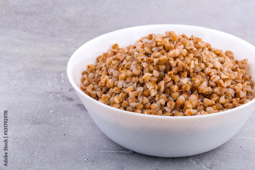 Cooked buckwheat in white ceramic bowl on grey background. Close up, horizontal format. Cooked buckwheat in white ceramic bowl on grey background. Close up, horizontal format.