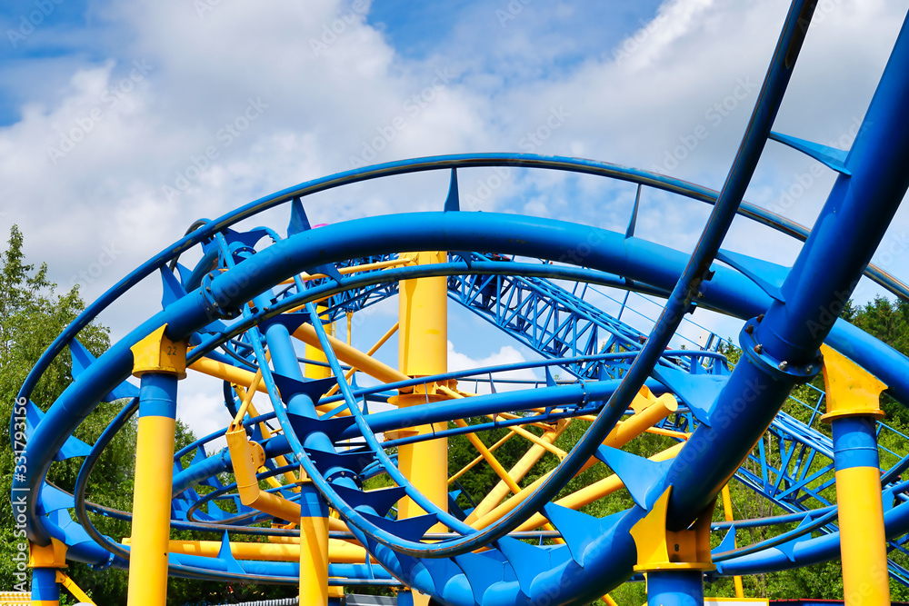 part of a rollercoaster with blue track and yellow support and blue sky with white clouds