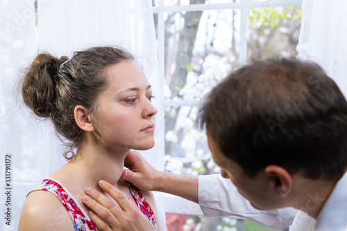 Doctor inspecting, doing palpation examination of young woman with Grave's disease hyperthyroidism symptoms of enlarged thyroid gland goiter and ophthalmopathy in hospital
