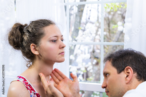 Male doctor inspecting, doing palpation examination of young woman with Grave's disease hyperthyroidism symptoms of enlarged thyroid gland goiter and ophthalmopathy in hospital