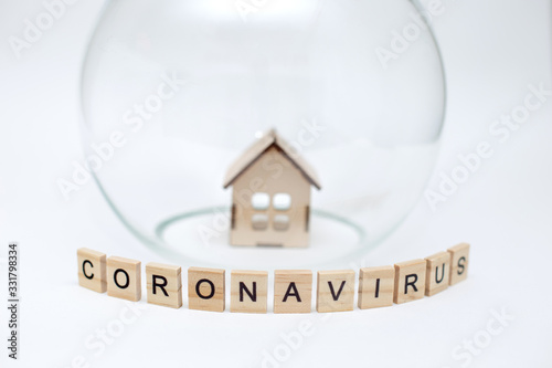 Model of a wooden house under a glass dome and wooden letters with the inscription Coronavirus ...