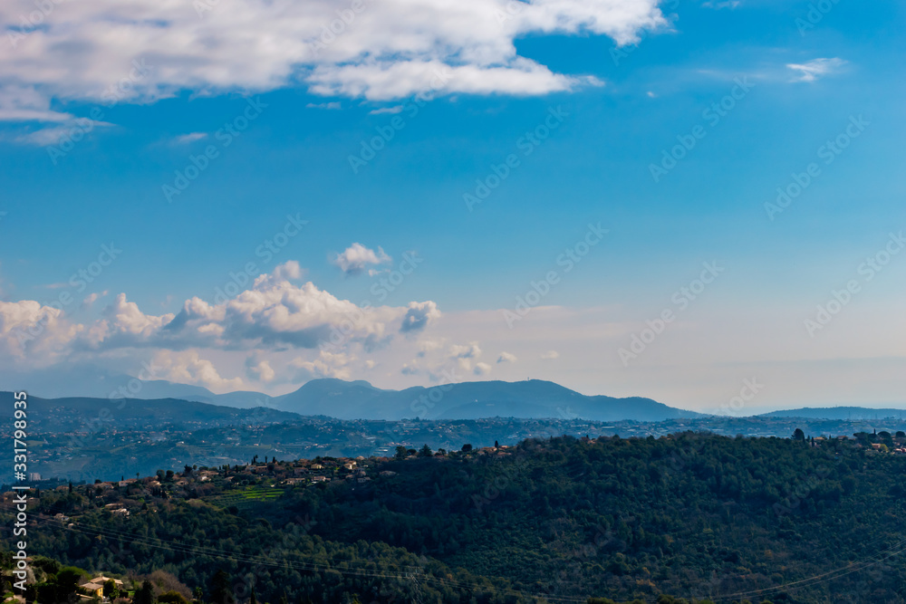 A wide / high angle panoramic view of the low Alps mountains hills covered with forests and remote buildings with hazy multilayered mountain ranges in background (French Côte d'Azur/Provence/Riviera)