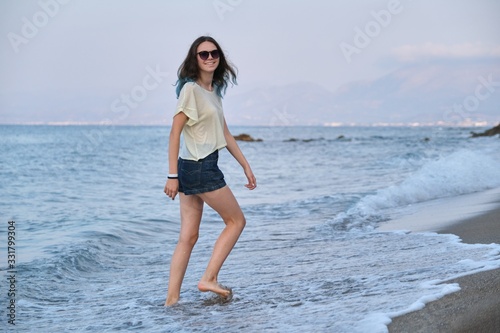 Fashionable young woman with dyed long blue hair walking along seashore