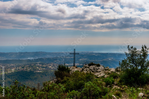 A metal cross installed on top of a cliff of the Baou des Noirs near Vence, France in the Alps mountains with the landscape and Mediterranean Sea in the background (Cote d'Azur / Provence)