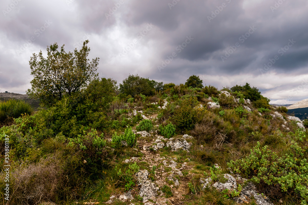 A hiking trail / footpath going up on top of a mountain range under the cloudy sky on a foggy afternoon in the low French Alps mountains