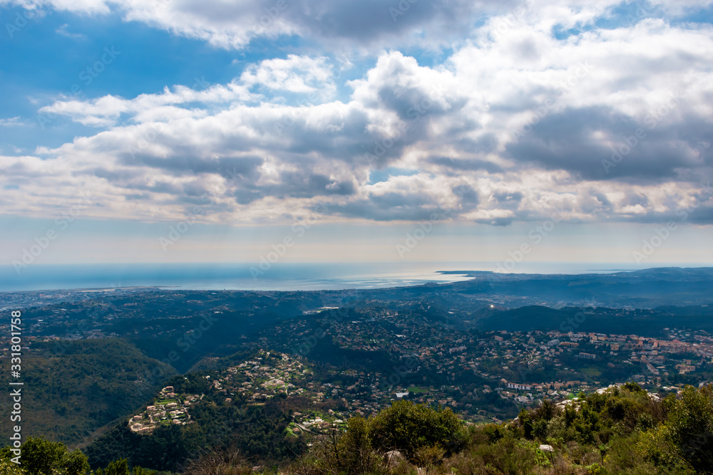 A panoramic view of several towns and their buildings densely covering the low Alps mountains hills with the Mediterranean Sea on the horizon (Provence / Riviera / Côte d'Azur)