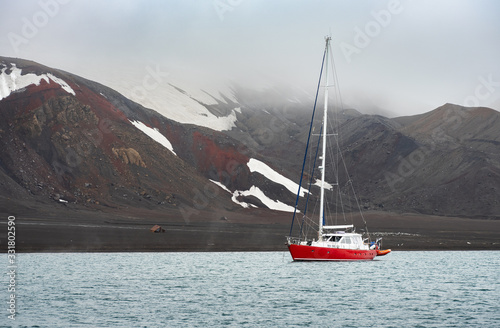 red sailing yacht on ancher in lagoon of volcanic island in Antarctica