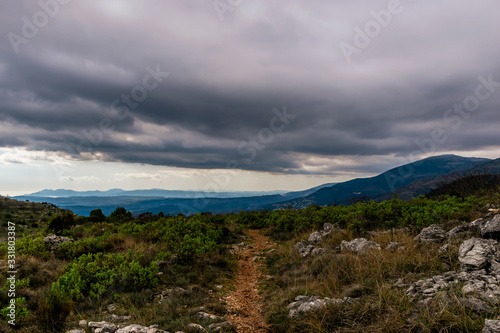 A hiking trail / footpath going straight on top of a mountain range under the cloudy sky on a foggy afternoon in the low French Alps mountains