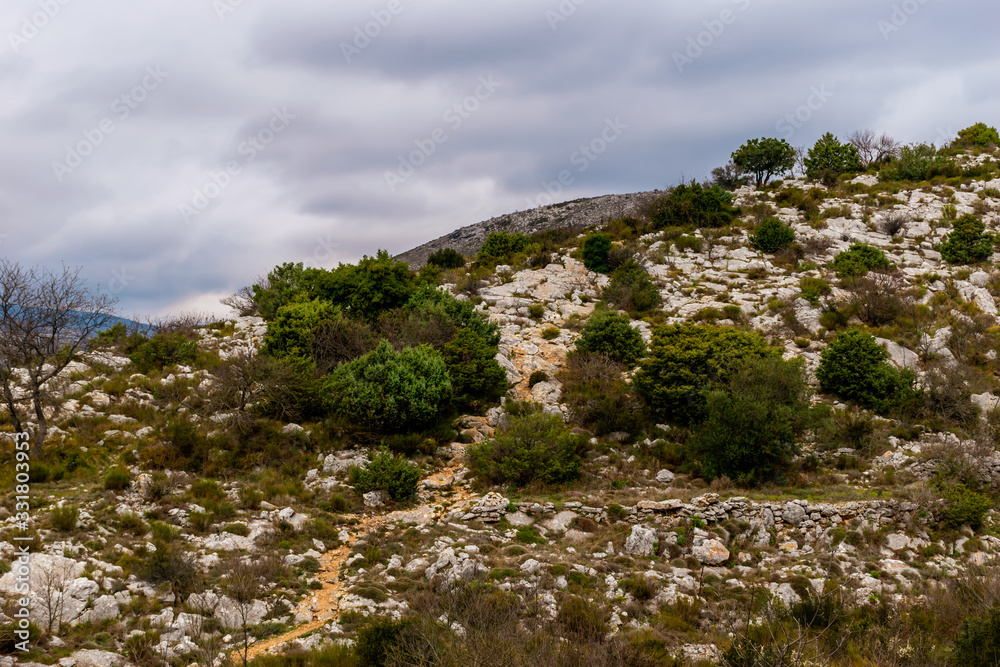 A hiking trail / footpath going up on top of a mountain range under the cloudy sky on a foggy afternoon in the low French Alps mountains A hiking trail / footpath going up on top of a mountain range under the cloudy sky on a foggy afternoon in the low French Alps mountains