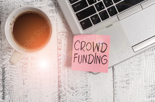 Conceptual hand writing showing Crowd Funding. Concept meaning technique of raising money from a large number of showing Trendy metallic laptop sticky note coffee cup on vintage table photo
