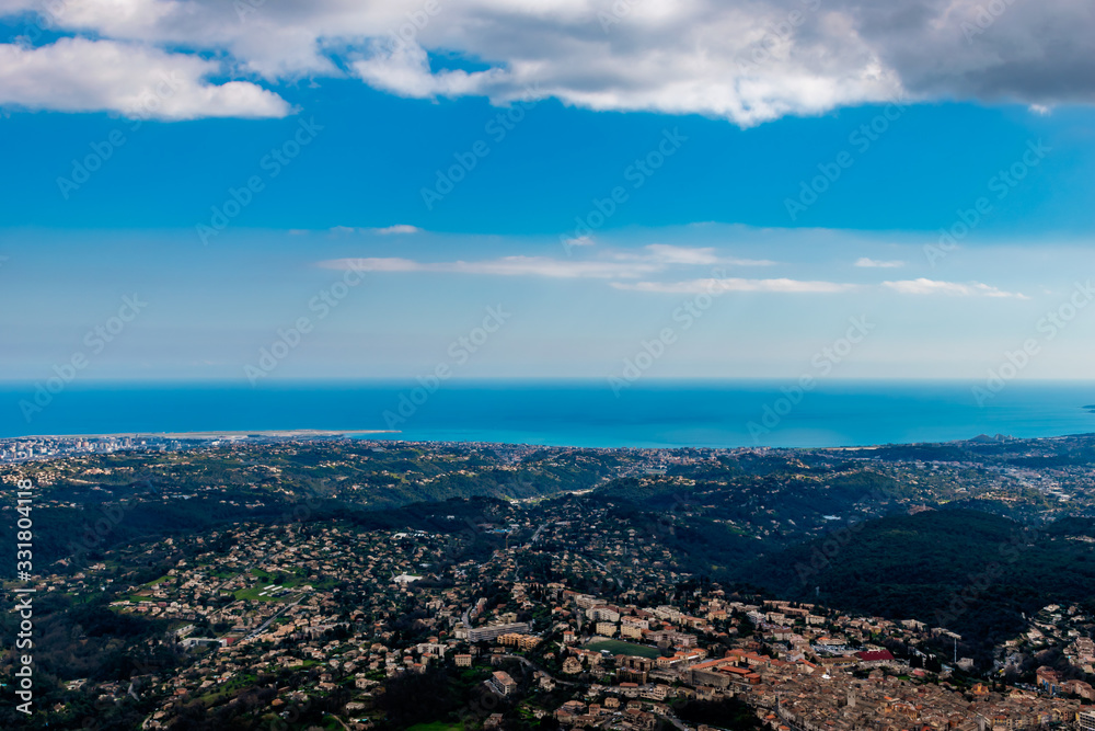 A wide / high angle panoramic view of buildings of several towns (including Vence) covering the low Alps mountains hills and the Mediterranean Sea coastline (French Côte d'Azur/ Provence/ Riviera)
