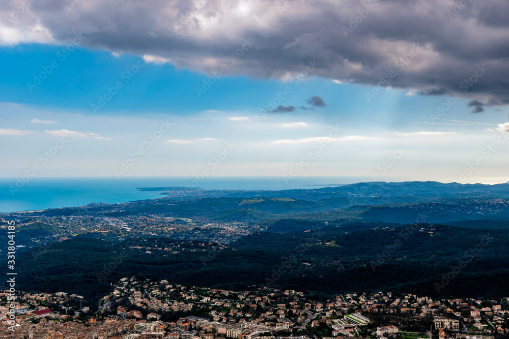 A wide / high angle panoramic view of buildings of several towns (including Vence) covering the low Alps mountains hills and the Mediterranean Sea coastline (French Côte d'Azur/ Provence/ Riviera)