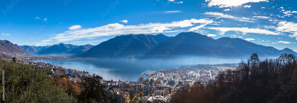Stunning aerial panorama view of  Locarno cityscape and Lake Maggiore from Madonna del Sasso church, snow covered Swiss Alps mountain and blue sky cloud in background in autumn, Ticino, Switzerland