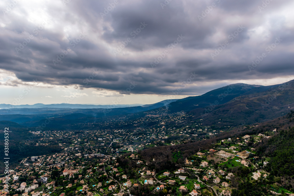 A wide / high angle panoramic view of houses and other buildings of several towns covering the low Alps mountains hills with the mountain ranges in the haze (French Côte d'Azur/ Provence/ Riviera)