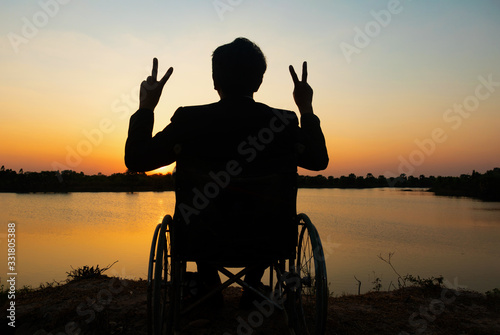 Silhouette young disabled man seeing river background.He is raise a hand to and sitting on wheelchair.Photo concept depression and Patient.