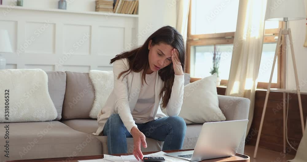 Upset young woman feeling stressed about financial debt checking bills at home. Frustrated lady doing paperwork sitting on sofa thinking of unpaid tax, bank loan, money problem or bankruptcy concept. Upset young woman feeling stressed about financial debt checking bills at home. Frustrated lady doing paperwork sitting on sofa thinking of unpaid tax, bank loan, money problem or bankruptcy concept.