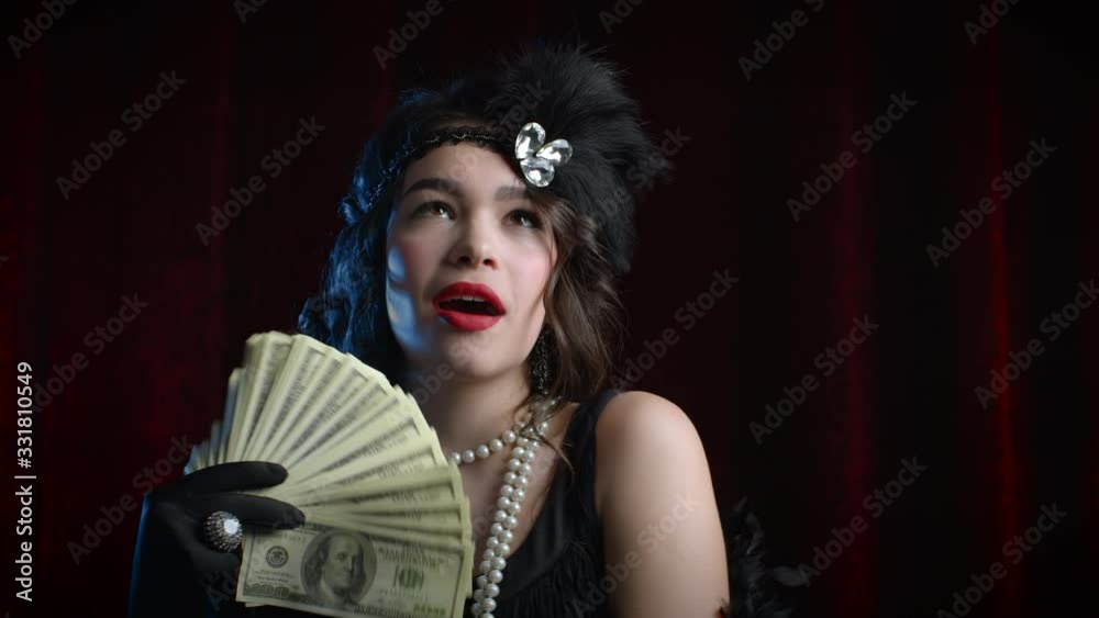 Rich luxurious woman dressed in Gatsby style waves a bundle of dollars banknotes like fan. Vintage, party, retro fashion concept. Rich luxurious woman dressed in Gatsby style waves a bundle of dollars banknotes like fan. Vintage, party, retro fashion concept.