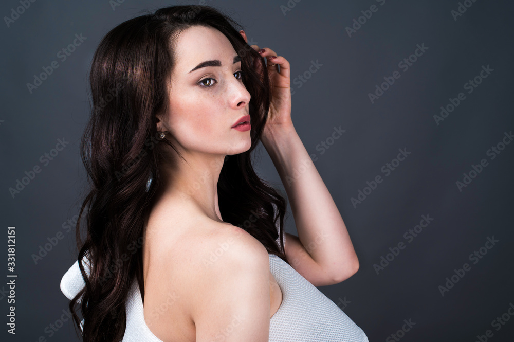 Portrait of the attractive young woman with perfect long hair posing at studio over dark background