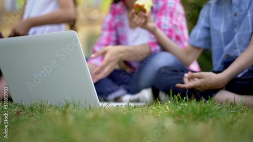 Close up on laptop, Mother with children in studdying outdoors. Teaching kids on air using a laptop, the son eating apple and daughter digging backpack selective focus. photo