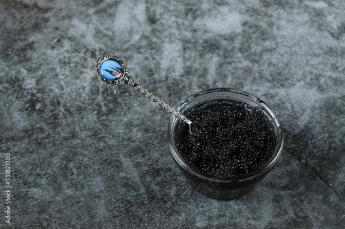 A glass jar with black caviar on a marble