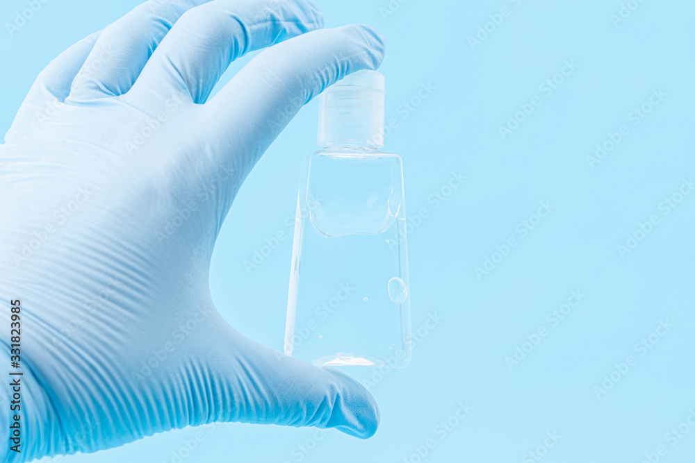 Hand with blue gloves holding a little bottle of sanitizer gel on blue background Hand with blue gloves holding a little bottle of sanitizer gel on blue background