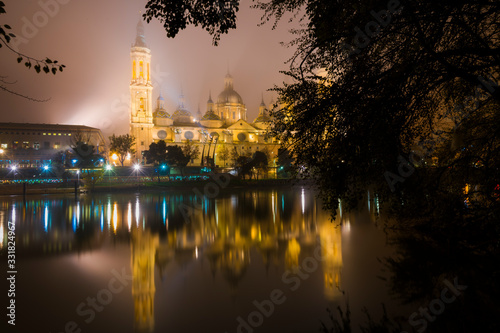 Church of our Lady of the Pillar in Zaragoza  Spain  illuminated at night with dense fog and reflections in the river