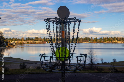 Disc golf basket on pretty park course near a lake under blue sky
