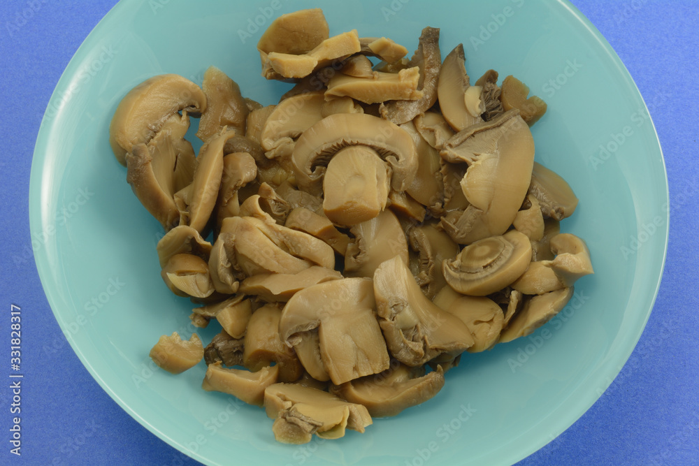 Close up on freshly rinsed canned mushrooms in blue bowl on darker blue background Close up on freshly rinsed canned mushrooms in blue bowl on darker blue background