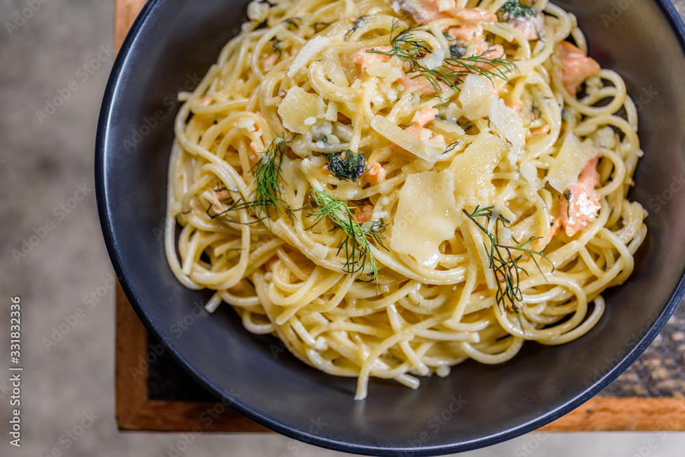A serving of Salmon Spaghetti in a plain blue round bowl on a wooden table A serving of Salmon Spaghetti in a plain blue round bowl on a wooden table