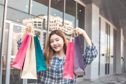 Smiling young Asian woman with shopping colour bags over mall background. using a smart phone shopping online and smiling while standing mall building. lifestyle concept
