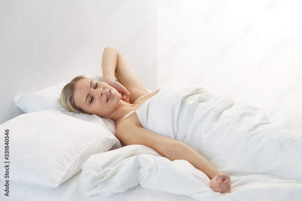 Young woman lying in the bed. Beautiful blond sleeping girl. Morning in the bedroom, daylight from the window. Health and rest. Young woman lying in the bed. Beautiful blond sleeping girl. Morning in the bedroom, daylight from the window. Health and rest.