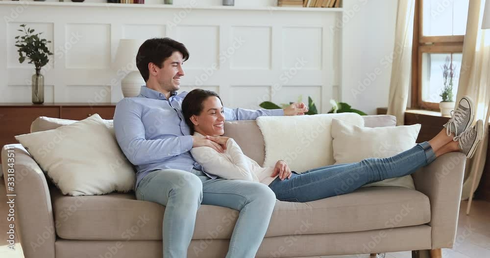 Happy relaxed young family couple bonding and talking sitting on comfortable sofa together. Carefree millennial man and woman enjoying lounge in cozy living room, chatting, relaxing on couch at home. Happy relaxed young family couple bonding and talking sitting on comfortable sofa together. Carefree millennial man and woman enjoying lounge in cozy living room, chatting, relaxing on couch at home.