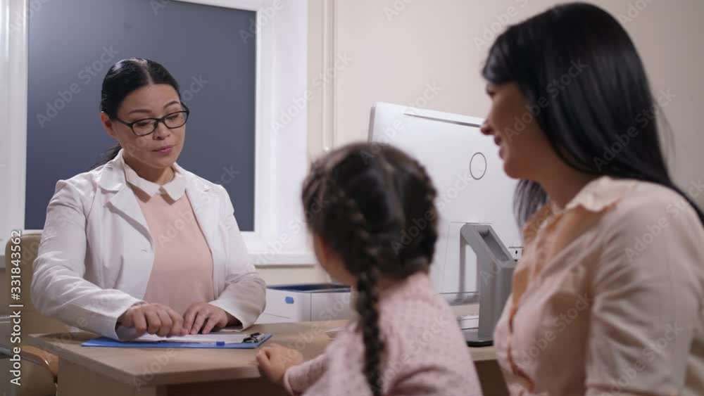 Close-up of positive female physician writing medical prescription for sick little girl and giving it to her mother. Smiling family doctor in glasses wishing small patient speedy recovery Close-up of positive female physician writing medical prescription for sick little girl and giving it to her mother. Smiling family doctor in glasses wishing small patient speedy recovery