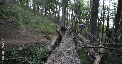 Young man hiking at wild woods, walking along fallen tree trunk. Old wild nothofagus forest at background. Patagonia, Argentina photo