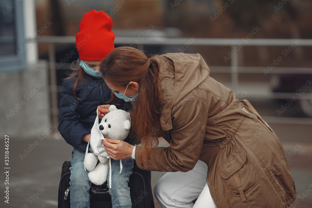 A European mother in a respirator with her daughter are standing near a building.The parent is teaching her child how to wear protective mask to save herself from virus. A European mother in a respirator with her daughter are standing near a building.The parent is teaching her child how to wear protective mask to save herself from virus.