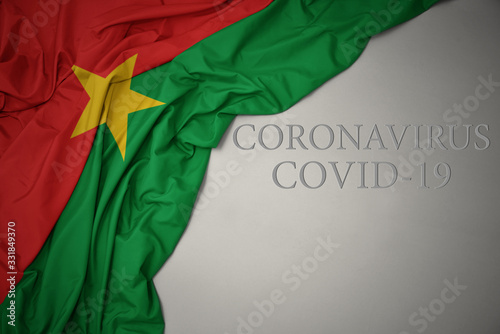 waving national flag of burkina faso on a gray background with text coronavirus covid-19 . concept.