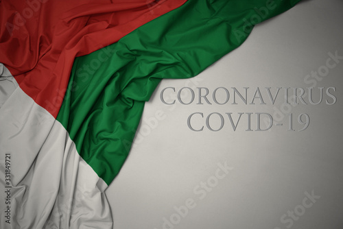 waving national flag of madagascar on a gray background with text coronavirus covid-19 . concept.