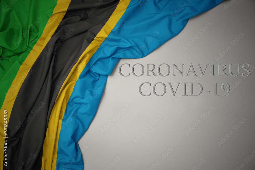 waving national flag of tanzania on a gray background with text coronavirus covid-19 . concept.