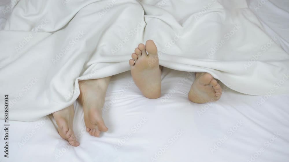 Young beautiful and loving couple playing and dancing their legs under the covers. Close-up of legs, top view