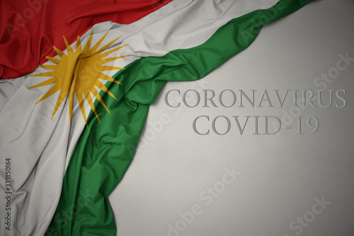 waving national flag of kurdistan on a gray background with text coronavirus covid-19 . concept.