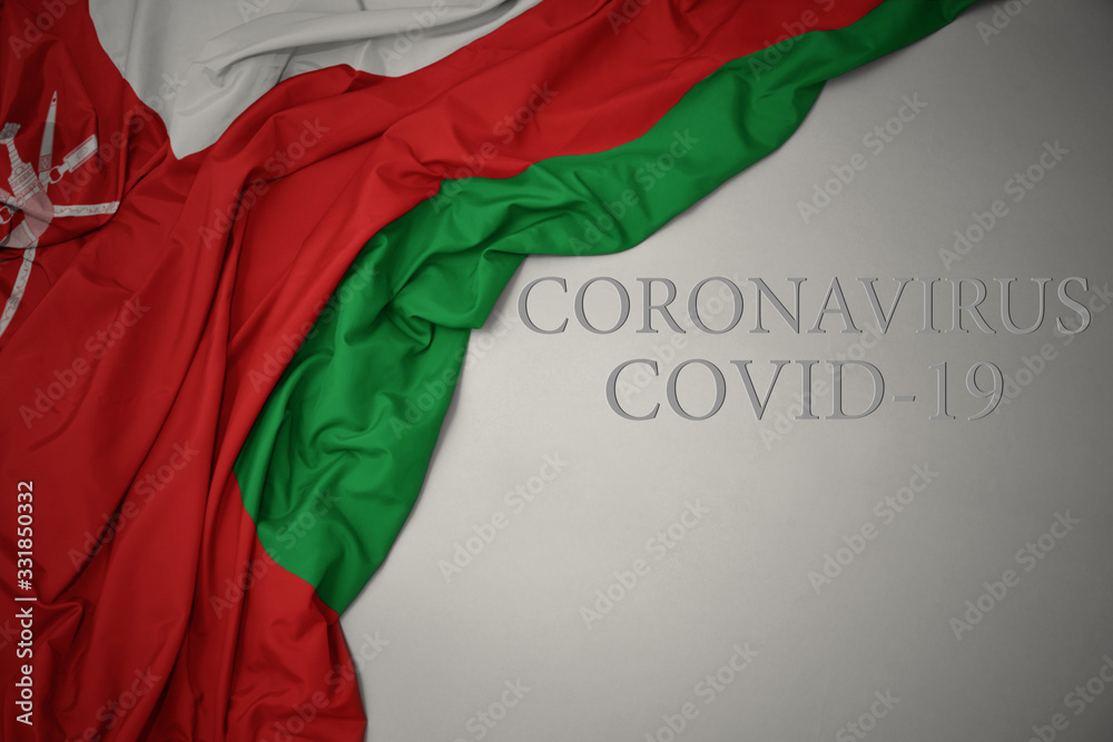 waving national flag of oman on a gray background with text coronavirus covid-19 . concept.
