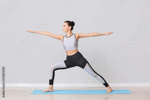 Young woman practicing yoga near light wall
