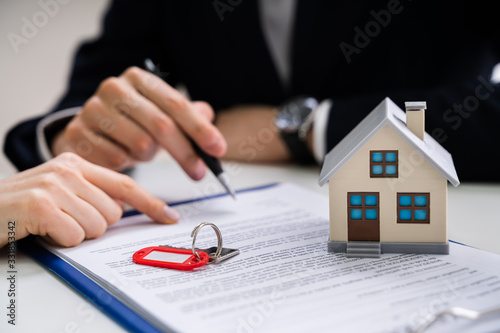 Person's Hand Signing Contract With Keys On It