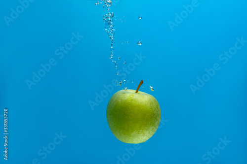 green apple falls into an aquarium with water on a blue background